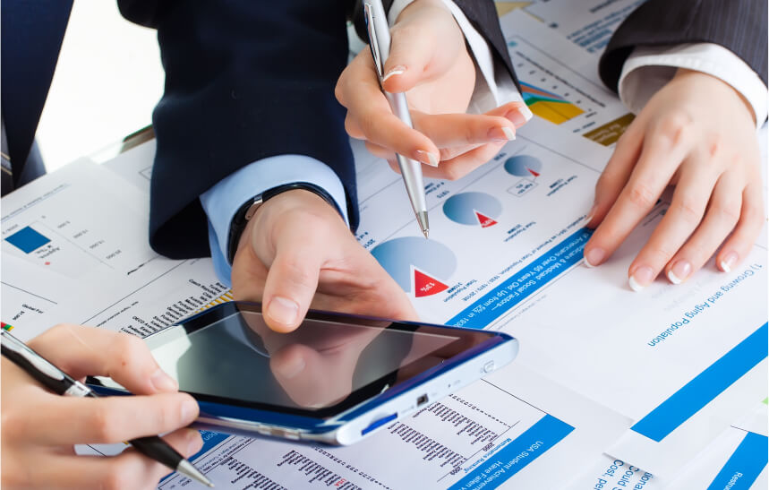 Business professionals discussing data and analyzing graphs with a smartphone and pen on top of financial reports.